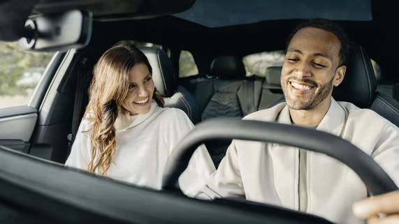 Eine Frau und ein Mann sitzen in einem Auto und scheinen sich freudig erregt auszutauschen.      