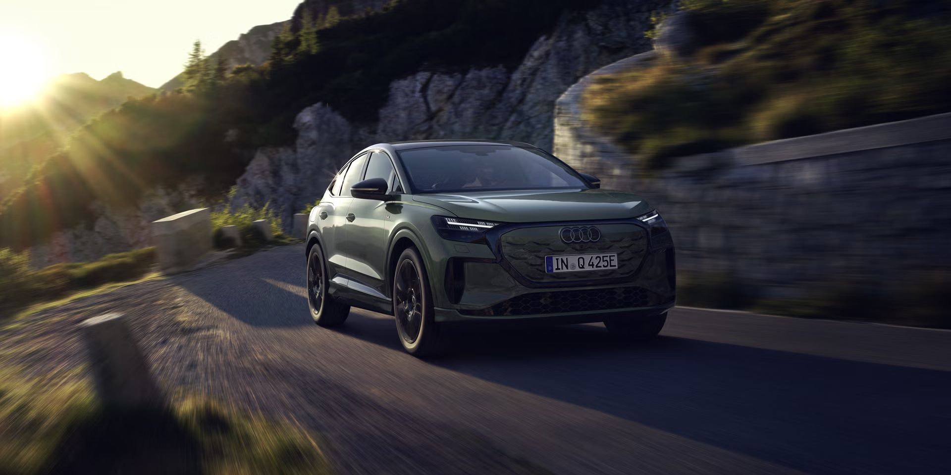 Der Q4 Sportback e-tron bei der Fahrt auf einer Bergstraße. Sonnenstrahlen von links oben beleuchten das Bild, das Fahrzeug wirft Schatten nach vorne.